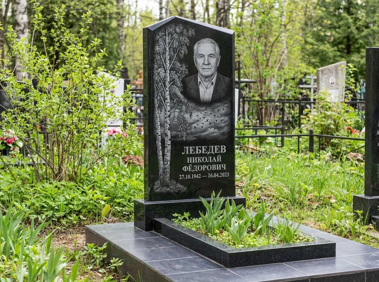 Памятник с гравировкой берёзы: вертикальная стела со скошенным верхом — берёза и стая птиц в небе, гранитный цоколь с тёмной плиткой, работа «Лебедев» в Сургуте