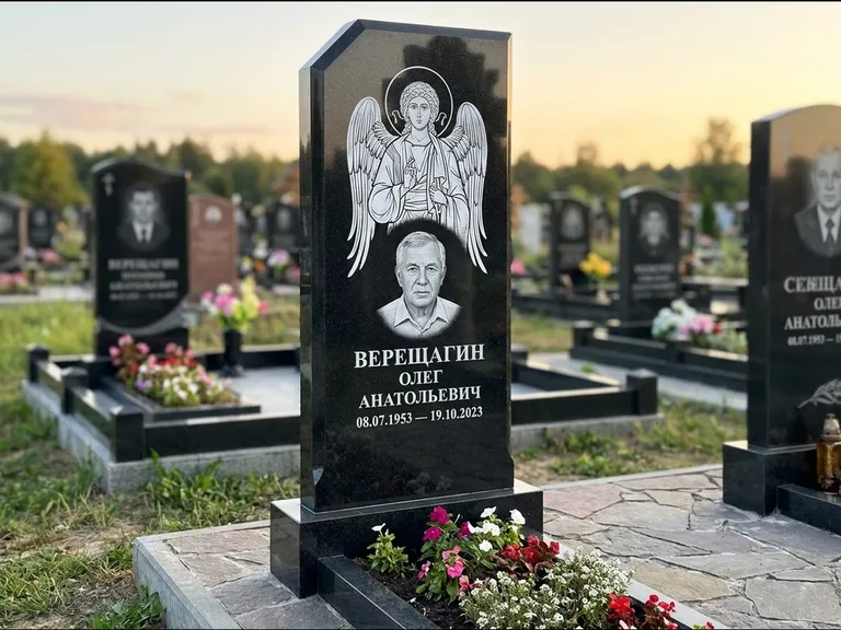 Памятник с гравировкой иконы: стела с резным навершием и нимбом в золоте — гравировка образа Спасителя, высокие разросшиеся туи полукругом, работа «Мельникова» в Сургуте