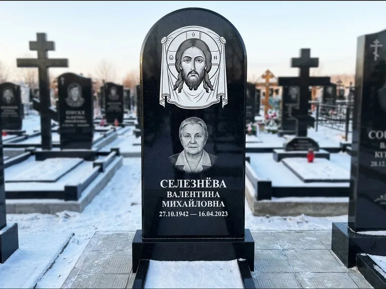 Памятник с гравировкой иконы: небольшая скромная одиночная стела с именной иконой — золочёный нимб на образе, аккуратный участок с газоном, работа «Ковалёв» в Сургуте