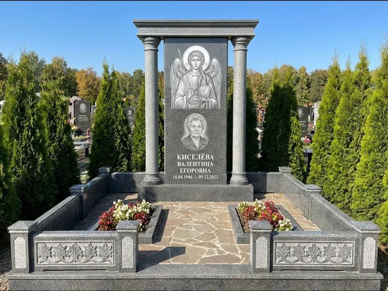 Памятник с гравировкой иконы: массивная стела с двускатным навершием-домиком — гравировка Николая Чудотворца, живая изгородь из туи, работа «Журавлёв» в Сургуте
