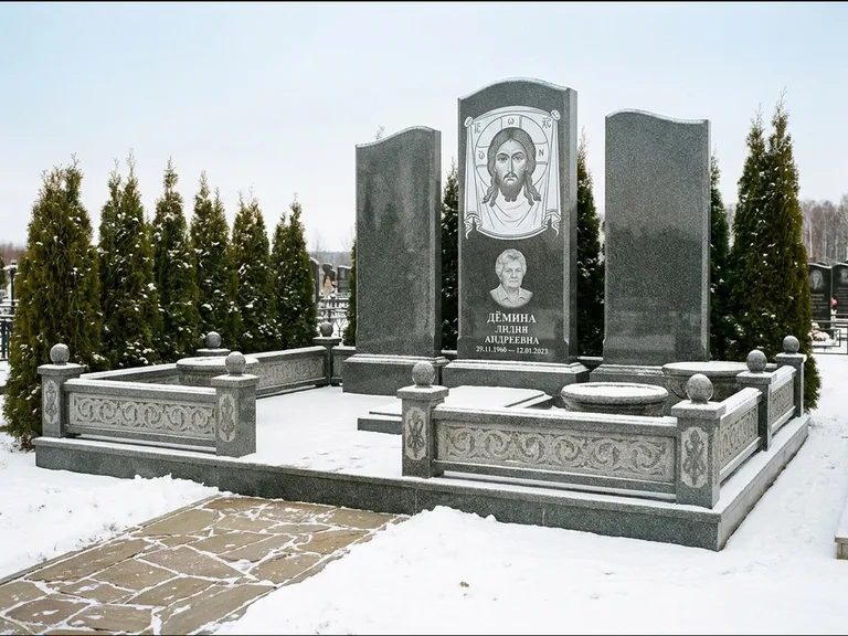 Памятник с гравировкой иконы: узкая вертикальная стела-пилон с ликом — икона в резной рамке-киоте, открытая лужайка без ограды, работа «Одинцов» в Сургуте