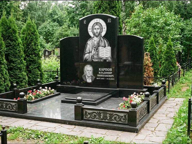 Памятник с гравировкой иконы: широкая панорамная стела с золочёным нимбом — гравировка образа Матроны Московской, цветник с белыми хризантемами, работа «Мельникова» в Сургуте