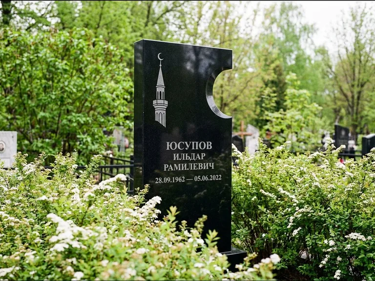 Мусульманский памятник с гравировкой мечети: стела с боковым вырезом в форме полумесяца — гравировка минарета с полумесяцем, низкие кусты спиреи в цвету, работа «Юсупов» в Сургуте