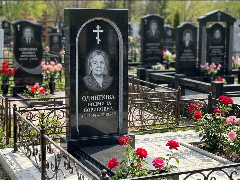Памятник из чёрного гранита — скромная невысокая стела с крестом с терновым венцом, работа «Лаврентьева» в Сургуте